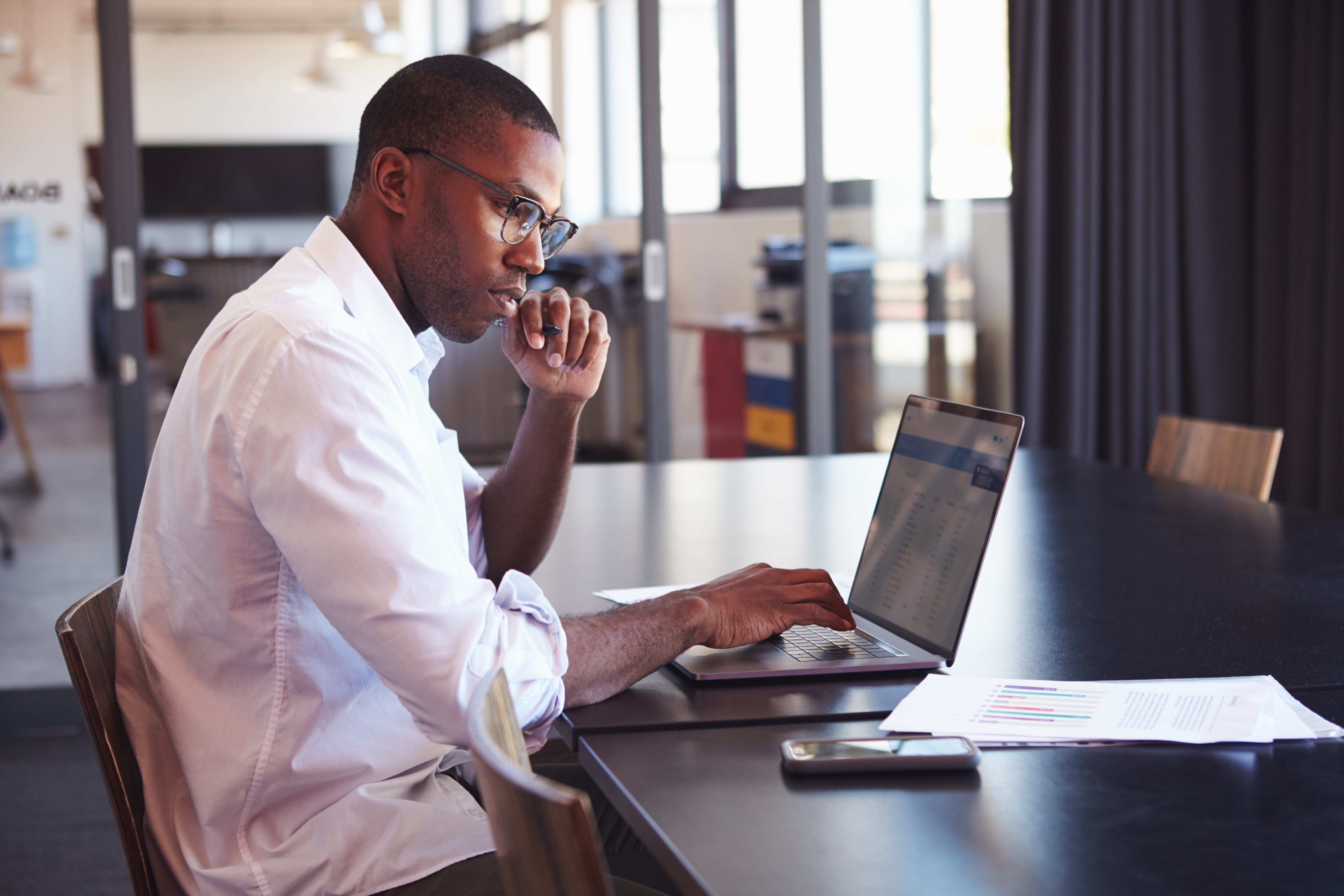 Young black man wearing glasses using laptop in office